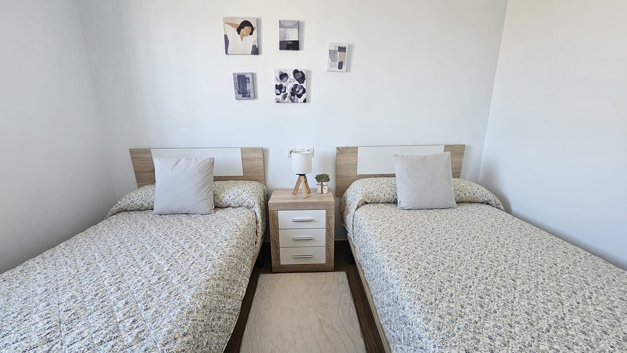 Habitación doble con cama, mesita de noche, lámpara y decoración en la pared.