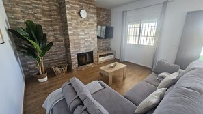 A living room with a brick fireplace, a flat-screen TV, a sofa, and a large window with curtains.