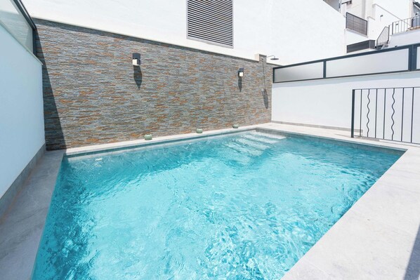 Ein rechteckiger Pool mit einer Steinwand auf der einen Seite und einer weißen Wand auf der anderen.
