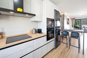 Une cuisine moderne équipée d’un four encastré, d’un réfrigérateur et d’un coin repas avec des tabourets de bar.