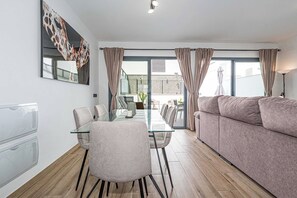Un salon moderne avec une table à manger en verre, un canapé et un balcon agrémenté de rideaux.