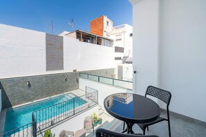 Área de piscina no terraço com guarda-corpo de vidro, mesa redonda com cadeiras e céu azul claro.