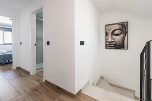 Um corredor com piso de madeira, uma escada e uma porta que dá para um quarto com cama.