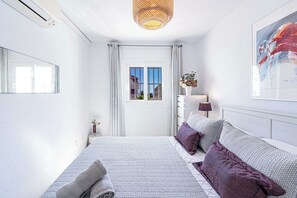 Ein Schlafzimmer mit einem Bett, einem Nachttisch, einer Lampe, einem Fenster und einem Bild an der Wand.