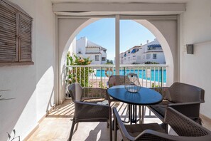 Ein Balkon mit Tisch und Stühlen, der einen Blick auf ein Schwimmbad und Gebäude bietet.