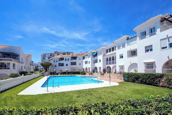 A pool area with a clear blue sky, surrounded by white buildings with balconies and arched windows. - Modern 2-bed, 2-bathroom by the pool,  Las Fuentes de Nerja (Nerja)