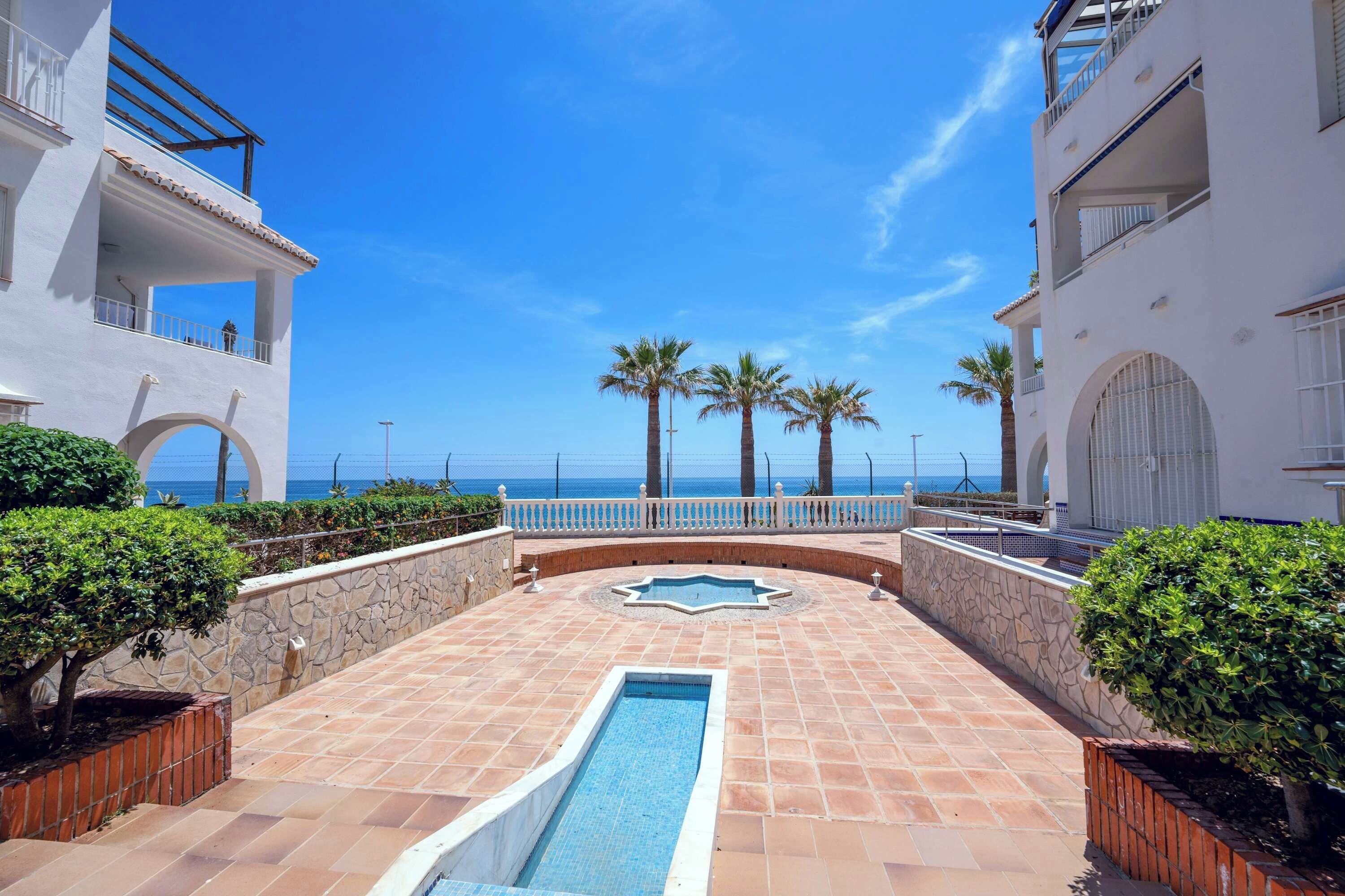 A pool area with a clear view of the sea, surrounded by white buildings with balconies.