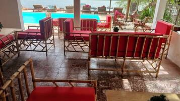 Zona junto a la piscina con mobiliario de mimbre y vista al mar.