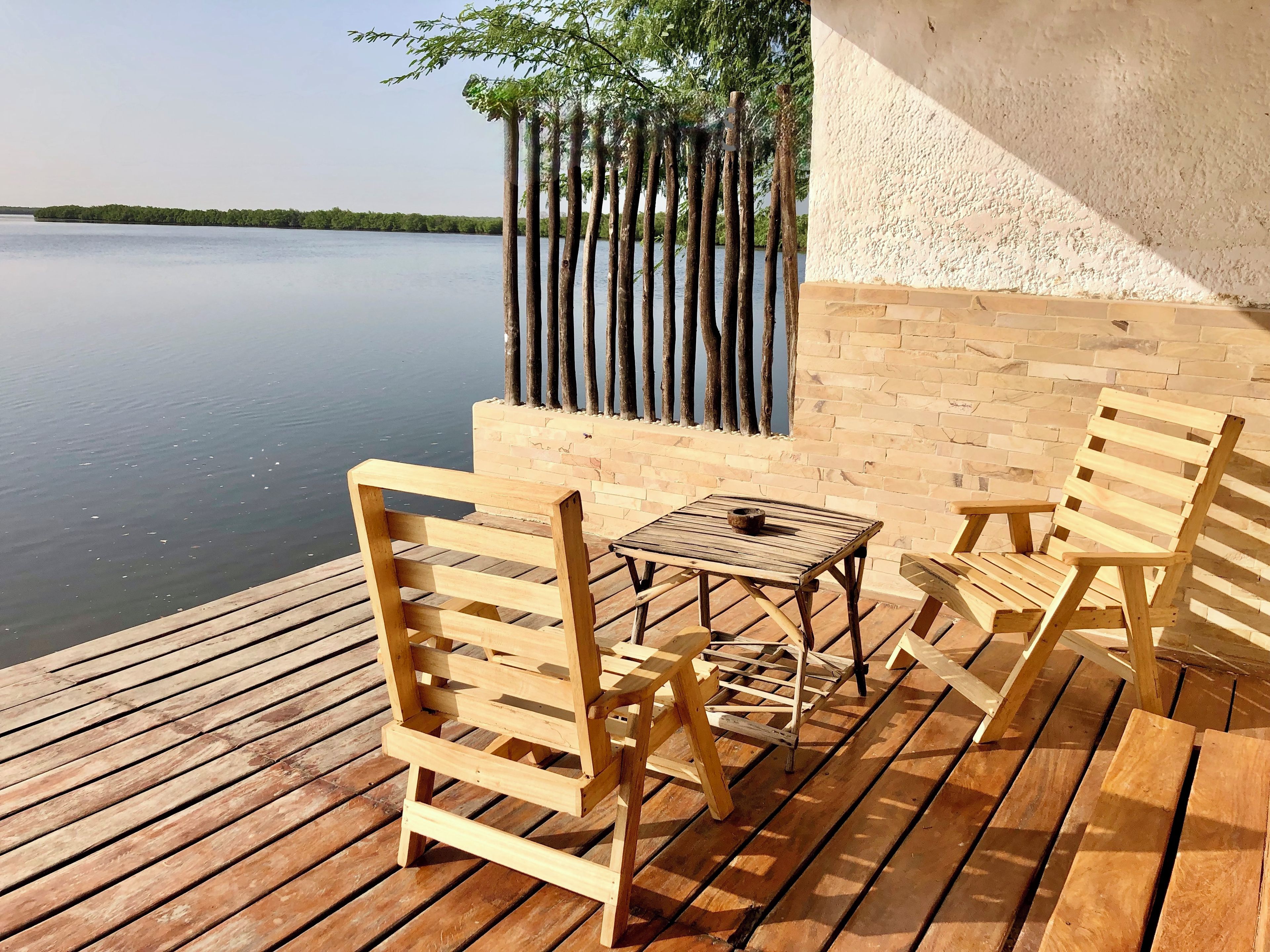 A wooden deck with a table and chairs, overlooking a calm body of water.