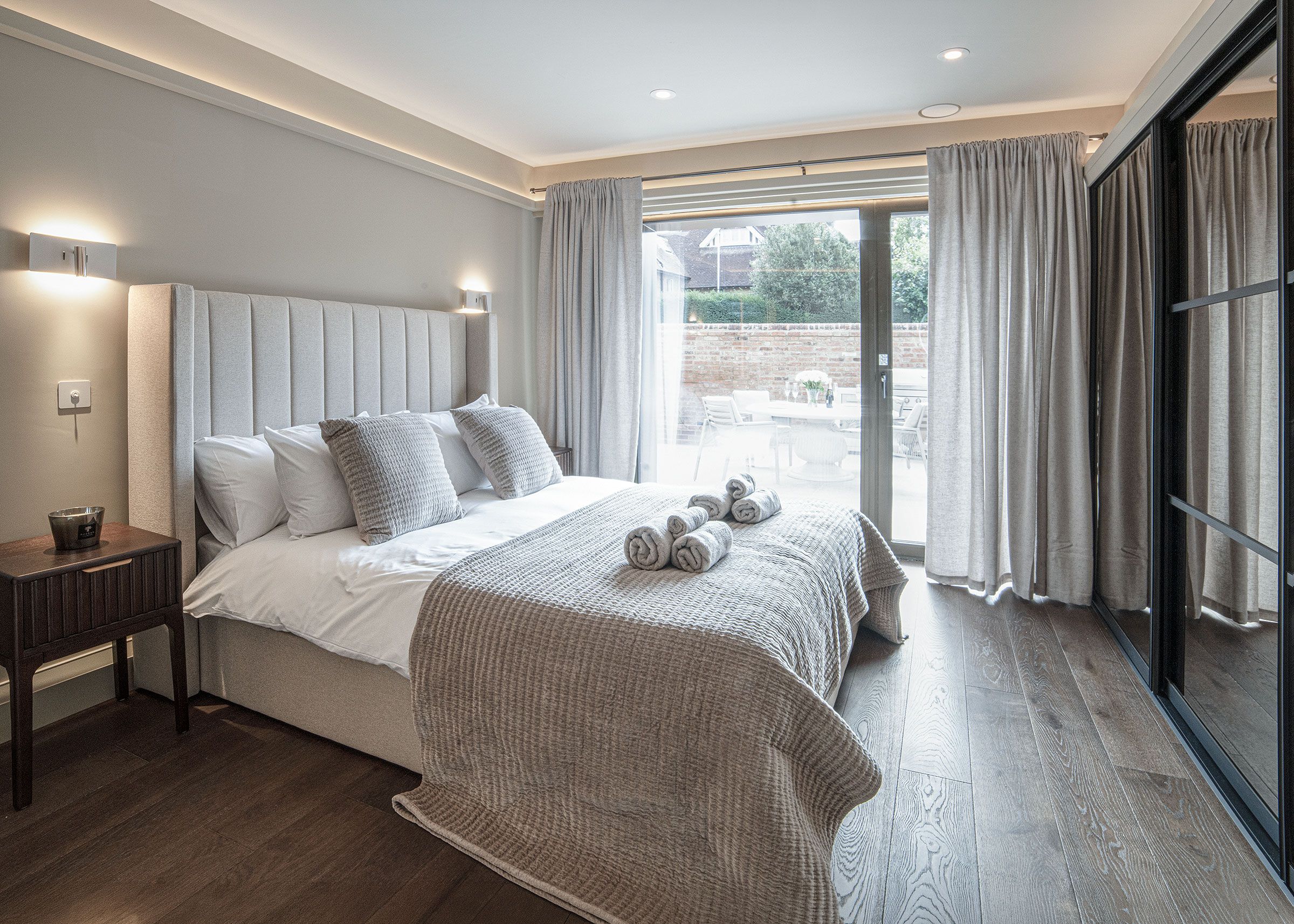 A bedroom with a large bed, a bedside table, a window with curtains, and a view of the outdoors.
