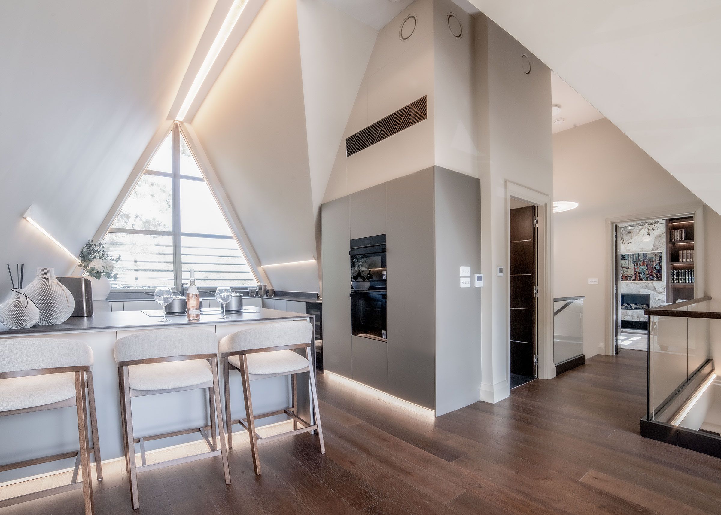 A modern kitchen with a bar area, wooden flooring, and a large window providing natural light.