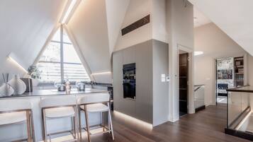 A modern kitchen with a bar area, wooden flooring, and a large window providing natural light.