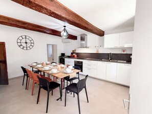 A modern kitchen with white cabinets, a wooden ceiling, and a dining area with a table set for four. - Le Mas de Menard (Barbentane)
