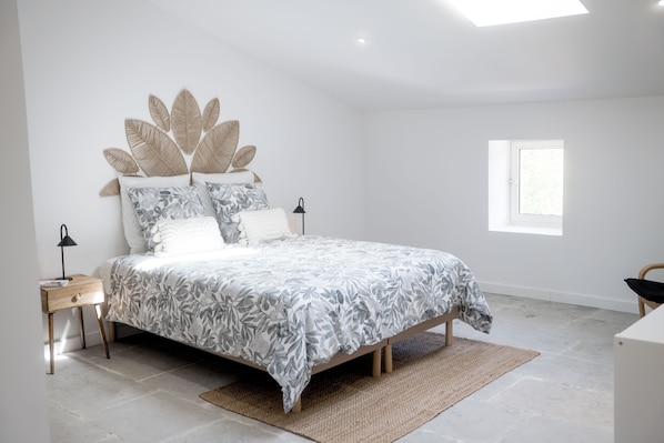 A bedroom with a bed, a bedside table, a lamp, a window, and a wall with a leaf-patterned headboard. - Le Mas de Menard (Barbentane)