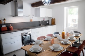 Eine moderne Küche mit weißen Schränken, einem eingebauten Backofen und einem Essbereich für sechs Personen mit einem Holztisch und Stühlen.