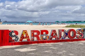 A beach with a sign spelling 'BARBADOS' and a clear sky.