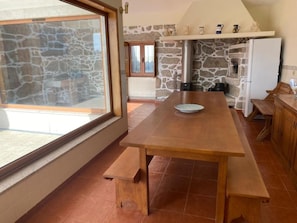 A kitchen with a wooden table, stone wall, and a view through a glass door. - Casa do Laranjal (Curvos)