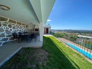 A balcony with a stone wall, outdoor seating, and a view of a swimming pool and landscape. - Casa do Laranjal (Curvos)