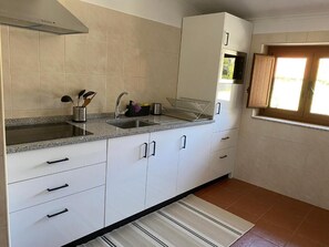 Una cucina con mobili bianchi, un piano di lavoro in granito, un lavello in acciaio inox e una finestra con persiane in legno.