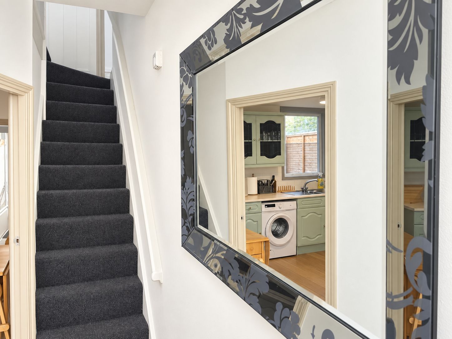 A staircase leading to a kitchen with a washing machine and a window.