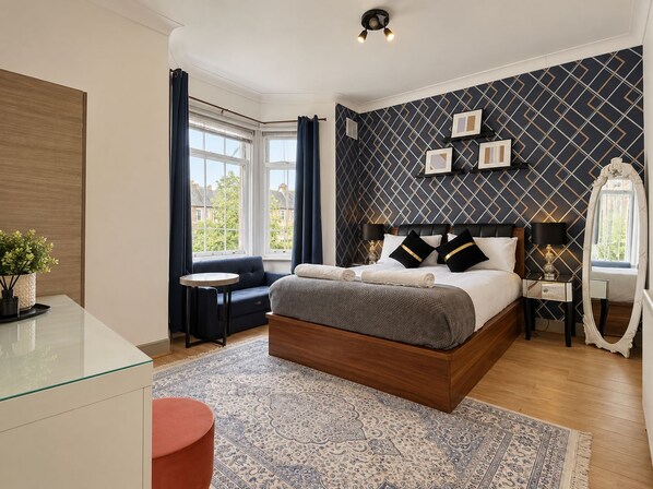 A modern bedroom with a large bed, a bedside table, a small round table, a sofa, and a large mirror.