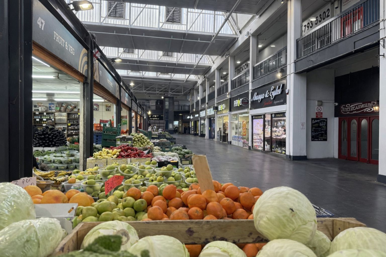 An indoor market with various stalls selling fruits and vegetables.