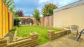 Een achtertuin met gazon, houten schutting, tuinhuisje en een tafel met stoelen.