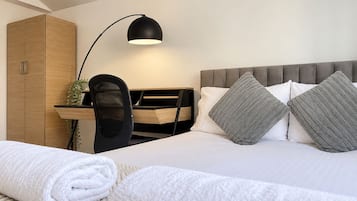 A hotel room with a bed, a desk, a chair, a wardrobe, and a lamp.