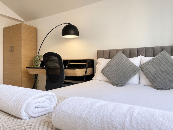 Una habitación de hotel con cama, escritorio, silla, armario y lámpara.