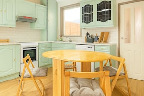 A kitchen with light green cabinets, a white stove, and a wooden table with cushioned chairs.