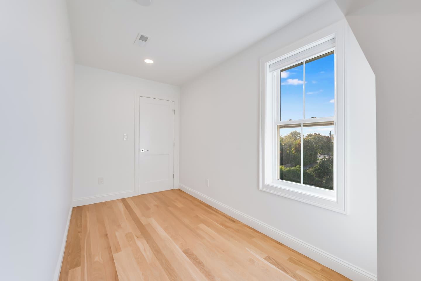 Une pièce dotée d’une grande fenêtre, de murs blancs et d’un plancher en bois.