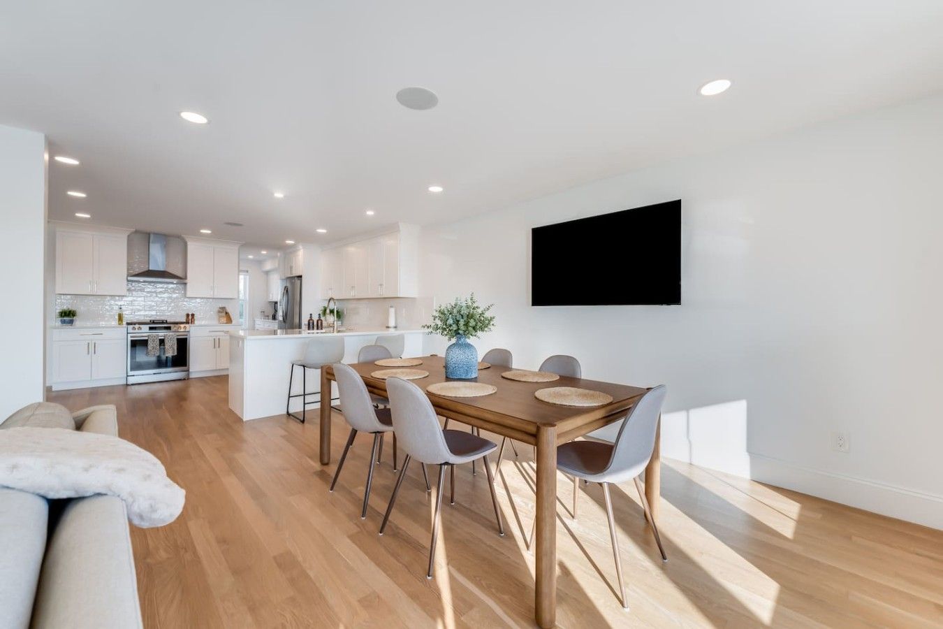 Een moderne keuken met witte kasten, een centraal eiland en een eethoek met een houten tafel en stoelen.