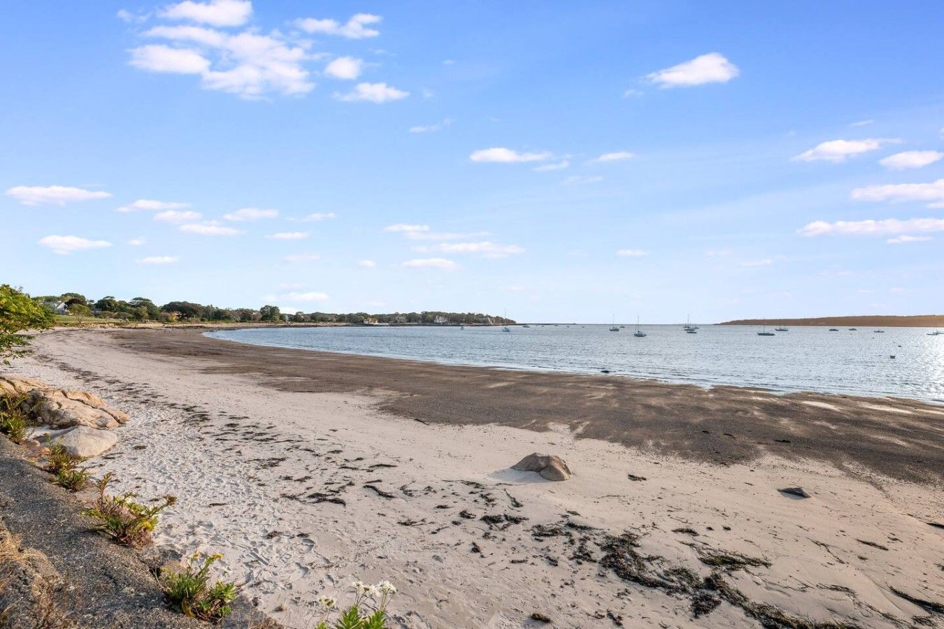 En strand med klar himmel, stilla vatten och båtar i fjärran.