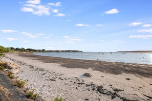 En strand med klar himmel, stilla vatten och båtar i fjärran.