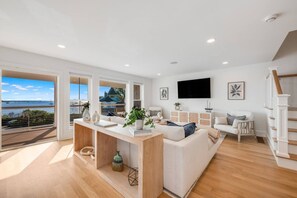 A spacious living area with a large window overlooking a scenic view, a wooden floor, and a white sofa. - Luxury Portside Townhome Steps to Niles Beach (Gloucester)