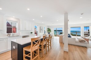 A modern kitchen with a central island, wooden chairs, and a view of the sea. - Luxury Portside Townhome Steps to Niles Beach (Gloucester)