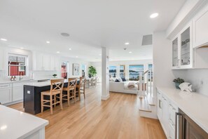 Een moderne keuken met witte kasten, een centraal eiland met barstoelen en uitzicht op de omgeving.