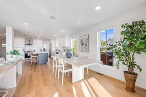 A modern kitchen with white cabinetry, a central island, and a dining area with a large table and chairs.