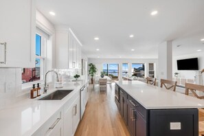 A modern kitchen with white cabinetry, a central island, and a view of the sea.