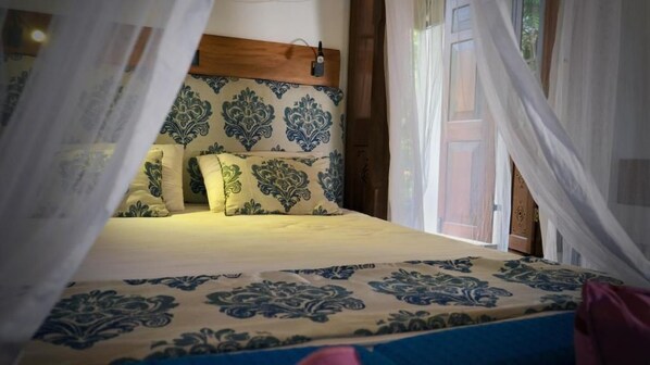 A bed with a patterned bedspread, a wooden headboard, and sheer curtains.