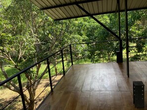 Una terraza de madera al aire libre con barandilla de metal, rodeada de árboles.