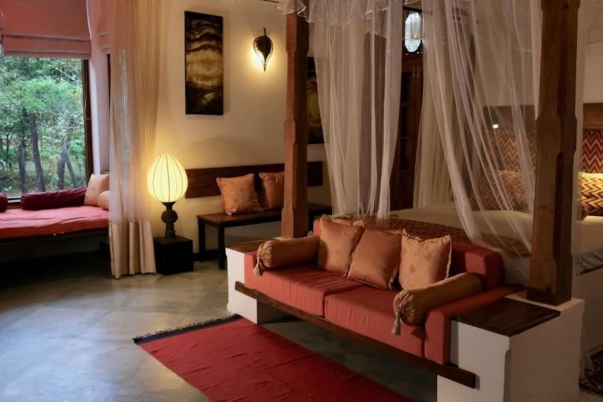 A room with a bed, a sofa, a nightstand, and a lamp.