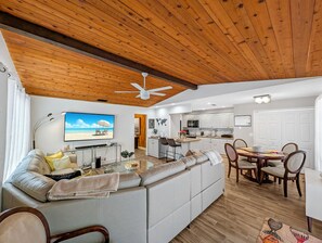 A modern living room with a large sofa, a dining area with a round table, and a kitchen with white cabinets. - Deerfield Coastal House - Cozy Stay (Deerfield Beach)
