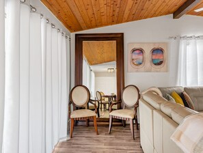 Une pièce avec un plafond en bois, un canapé beige, deux chaises en bois et une table à manger avec des chaises.