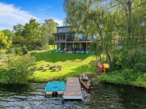 A modern house with a deck and outdoor seating, a dock with a boat, and a river. - Chapel Cove Waterfront Home near Whitewater Lake (Whitewater)