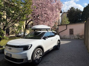 Een witte SUV geparkeerd op een keienpad, met een kersenboom op de achtergrond.