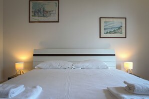 A neatly made bed with white linens and pillows, two bedside lamps, and two framed artworks on the wall. - LuxRent Penthouse in Crimea (Torino)