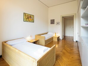 A room with two single beds, wooden flooring, and a door leading to another room. - Vrbo Property (Torino)