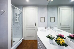 A modern bathroom with a glass shower enclosure, a large mirror, and a vanity with a sink and potted plants. - Vrbo Property (Torino)