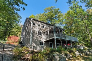 Une maison en bois à deux étages, dotée d’un balcon, entourée d’arbres et située dans un paysage rocheux.